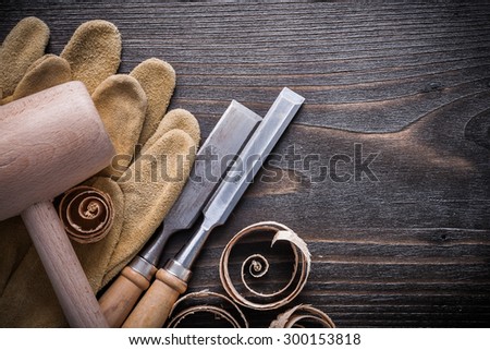 Brown leather gloves flat chisels wooden hammer and planning chips on vintage wood board construction concept.