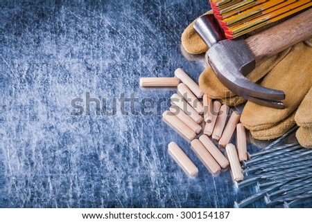 Claw hammer leather safety gloves wooden meter heap of metal nails and dowels on scratched metallic background construction concept.