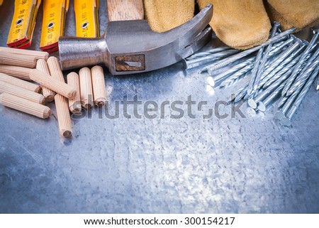 Claw hammer leather safety gloves wooden meter construction nails and dowels on scratched metallic background maintenance concept.