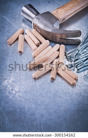 Claw hammer heap of construction nails and wooden dowels on scratched metallic background maintenance concept.