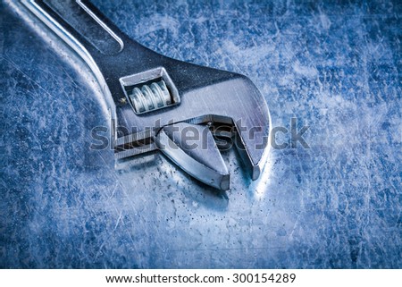 Close up version of stainless adjustable spanner on scratched metallic background construction concept.