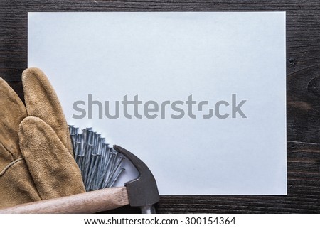 Blank sheet of paper steel nails claw hammer and leather protective gloves on vintage wooden board copy space construction concept.
