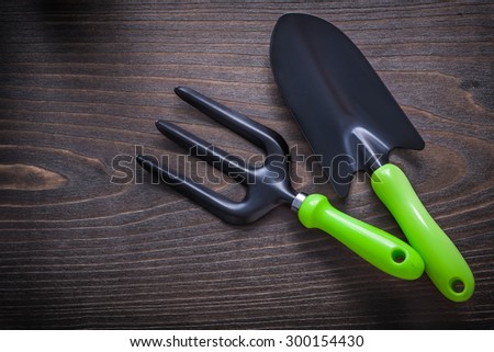 Black hand spade and trowel fork with green handles on vintage wooden background gardening concept.