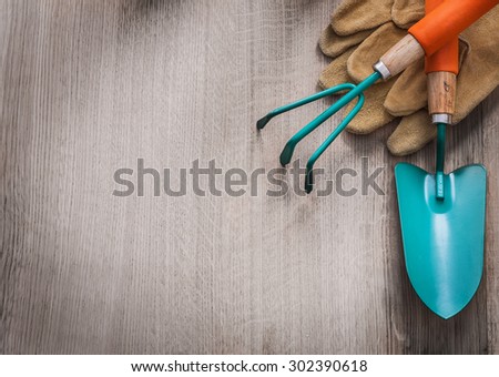 Pair of leather working gloves hand spade and gardening rake on wooden board agriculture concept.