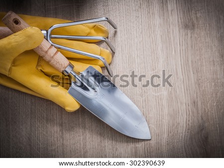 Stainless hand trowel rake yellow leather working gloves on wood board agriculture concept.