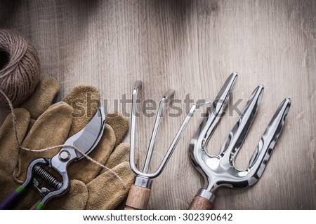 Gardening rake trowel fork leather safety gloves sharp metal secateurs and skein of twine on wooden background agriculture concept.