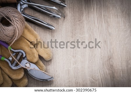 Composition of gardening rake metal trowel fork leather working gloves sharp garden pruner and hank of string on wood board agriculture concept.