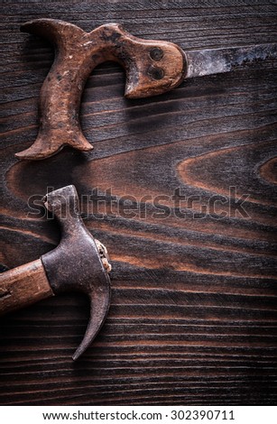 Rusty antique handsaw with claw hammer on vintage dark wooden background construction concept.