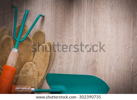 Leather gardening gloves metal hand spade and rake on wood board top view agriculture concept.