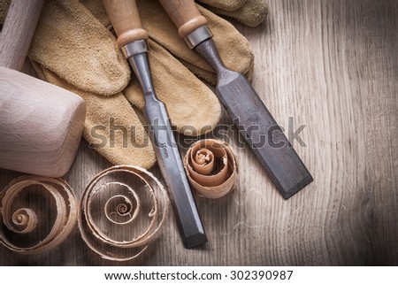 Wooden mallet curled up planning chips firmer chisels leather gloves on wood board construction concept.