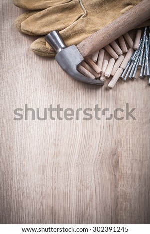 Wooden dowels claw hammer leather working gloves and stainless nails on wood board copy space construction concept.