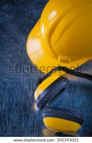 Protective yellow ear muffs and hard hat on scratched metallic background construction concept.