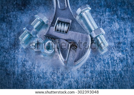 Steel adjustable spanner screw-nuts and threaded bolts on scratched metallic background construction concept.