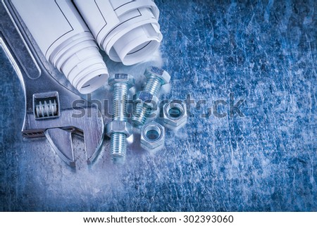 Steel adjustable spanner construction nuts bolts and rolls of blueprints on scratched metallic background maintenance concept.