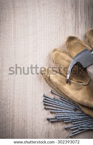 Vertical view of claw hammer leather protective gloves and steel long nails on wooden surface construction concept.