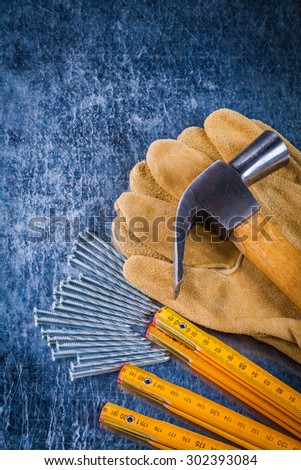 Set of leather working gloves nails wooden meter and claw hammer on scratched metallic background construction concept.
