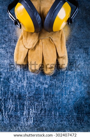Leather safety gloves and noise insulation ear muffs on scratched metallic background copy space image construction concept.
