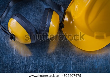 Noise reduction yellow headphones and work building helmet on scratched metallic background construction concept.