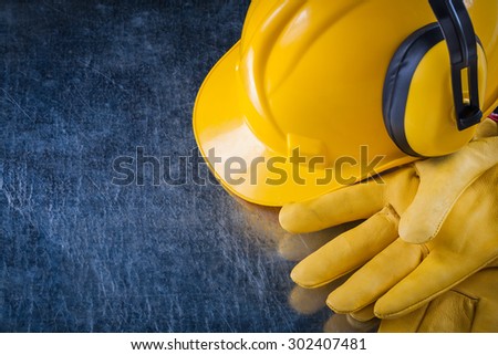 Hard hat safety ear muffs and yellow protective gloves on scratched metallic background construction concept.