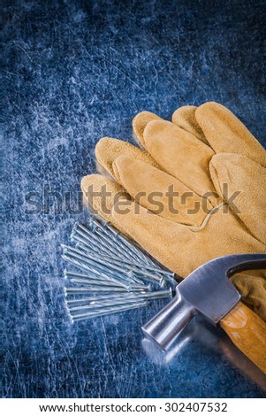 Leather protective gloves construction nails and claw hammer on scratched metallic surface building concept.