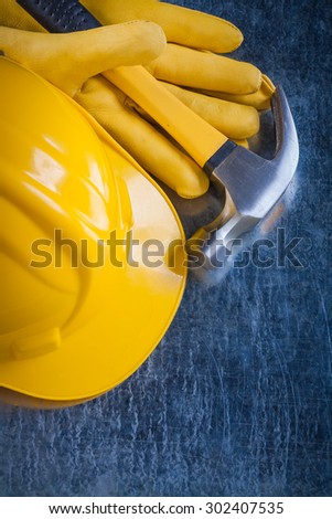 Leather yellow protective gloves building helmet and claw hammer on metallic surface construction concept.
