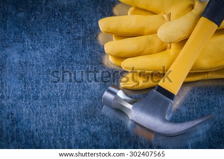 Leather protective work gloves with claw hammer on scratched metallic background construction concept.