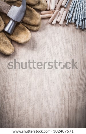 Heap of wooden dowels claw hammer leather working gloves and stainless nails on wood board top view construction concept.