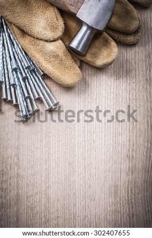 Claw hammer leather safety gloves and stack of stainless nails on wooden background construction concept.