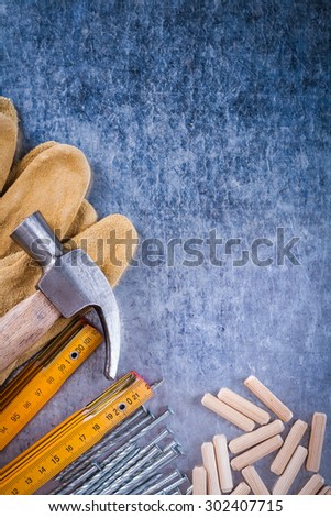Big set of claw hammer safety gloves wooden meter stainless nails and dowels on scratched metallic surface construction concept.