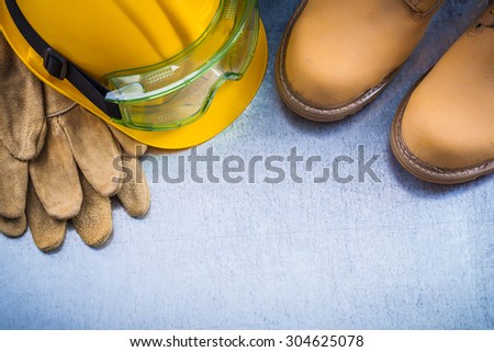 Set of brown safety waterproof shoes leather gloves hard hat and working glasses on scratched metallic background construction concept.