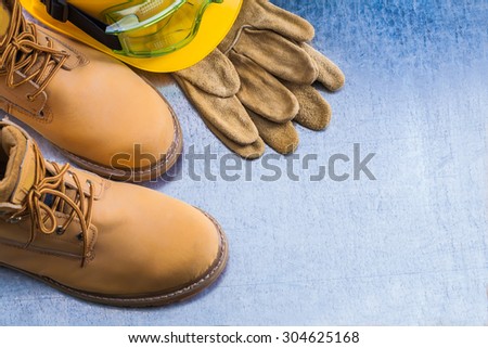 Pair of safety lace boots leather gloves hard hat and working goggles on scratched metallic background construction concept.