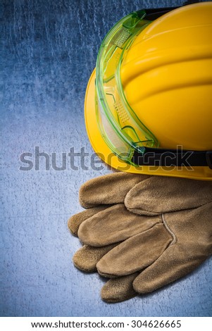 Composition of construction leather gloves building helmet and transparent goggles on scratched metallic background maintenance concept.
