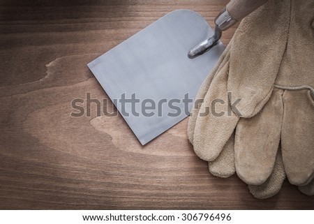 Working protective gloves and construction spattle on vintage wooden surface.