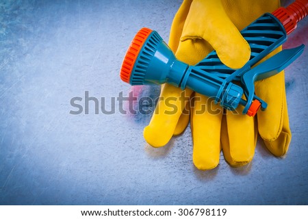 Leather safety gloves with hand spraying nozzle on metallic background.