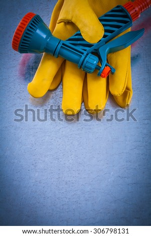 Leather protective gloves with hose spraying nozzle on metallic background.