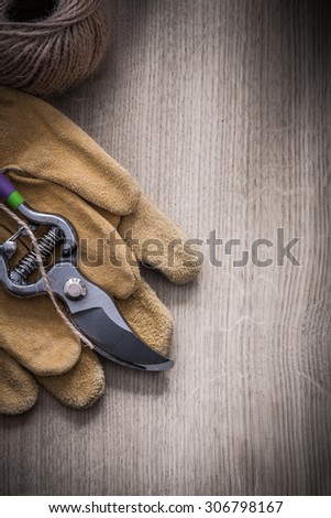 Pair of leather safety gloves sharp metal secateurs and skein of twine on wooden background agriculture concept.