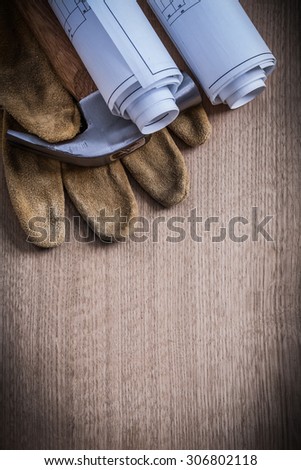 Construction plans safety gloves and claw hammer on wooden board.