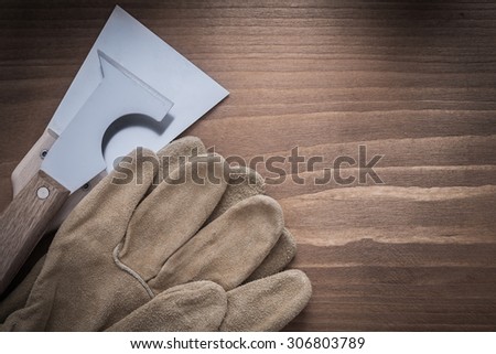Construction safety gloves and putty knives on wooden background.
