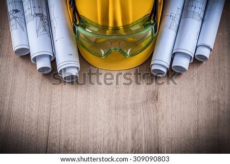 Protective glasses construction plans and building helmet on wooden surface.
