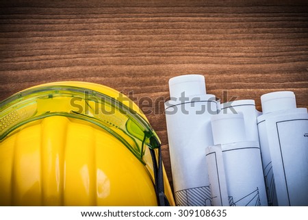 Protective spectacles construction plans and safety helmet on wooden surface.