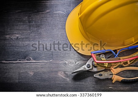 Building helmet safety glasses pliers tin snips on wooden background.