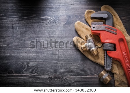 Pipe wrench plumbing fixtures protective gloves on wooden board.