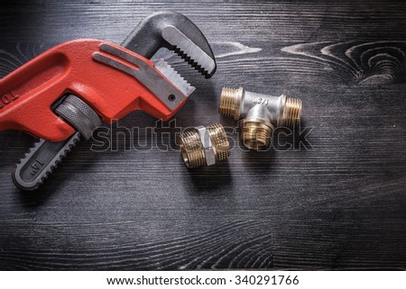 Monkey wrench brass plumbing fittings on wooden board.