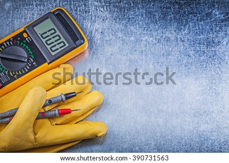 Digital electric tester safety gloves on metallic background electricity concept.