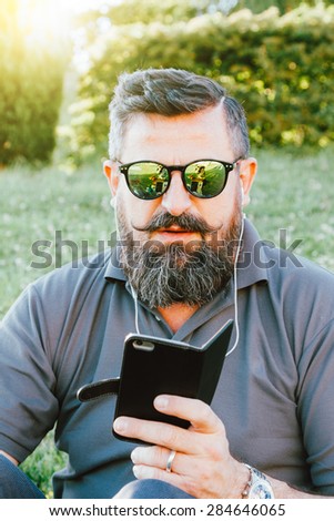 Adult hipster fashion man with smartphone sitting at the park - Concept of new trends and technology mixed with vintage lifestyle - Business man on retro nostalgic filtered look