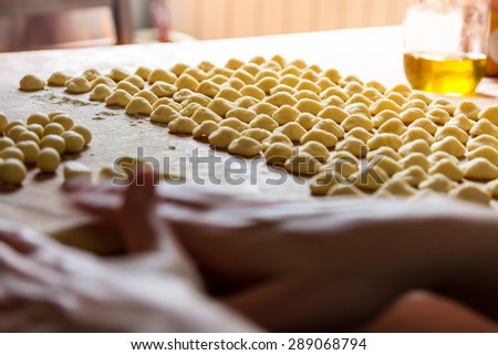 Female hands cooking fresh Italian hand made pasta, Orecchiette. \
Sun beam coming from the window on the background. Selective focus on the rows of pasta.