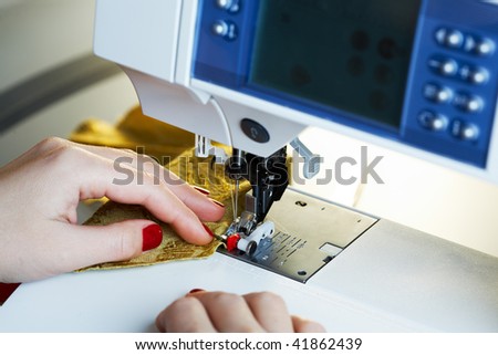 A hand of a dressmaker supporting a cloth while sewing on a sewing machine