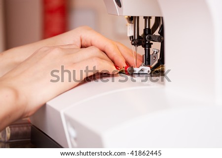 A hand of a dressmaker supporting a cloth while sewing on a sewing machine