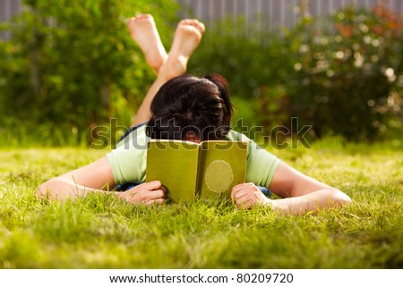 caucasian woman is reading the green book lying on the grass in the park