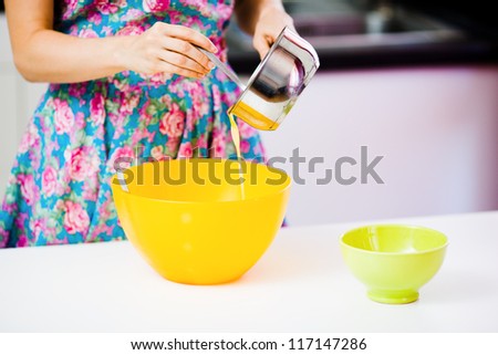 Pouring out melted butter from a metallic pot to an orange plastic bowl at homely kitchen